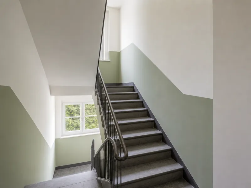 Renoviertes Treppenhaus mit salbeigrüner Akzentwand, Metallgeländer und Steinstufen.